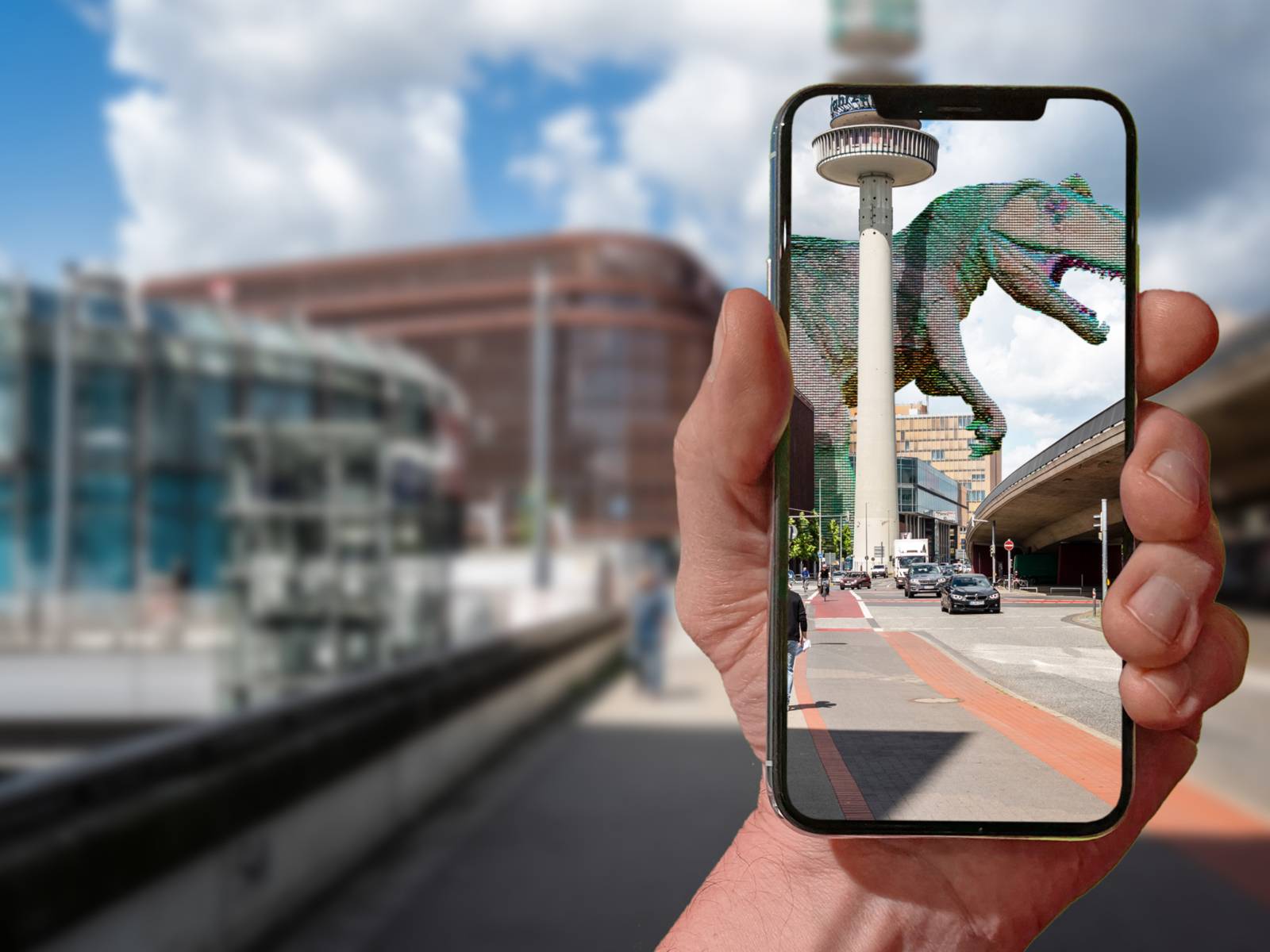 Eine Straße in Hannover. Davor hält eine Hand ein Handy. Über den Monitor wird ein Dino in die Straße eingeblendet.